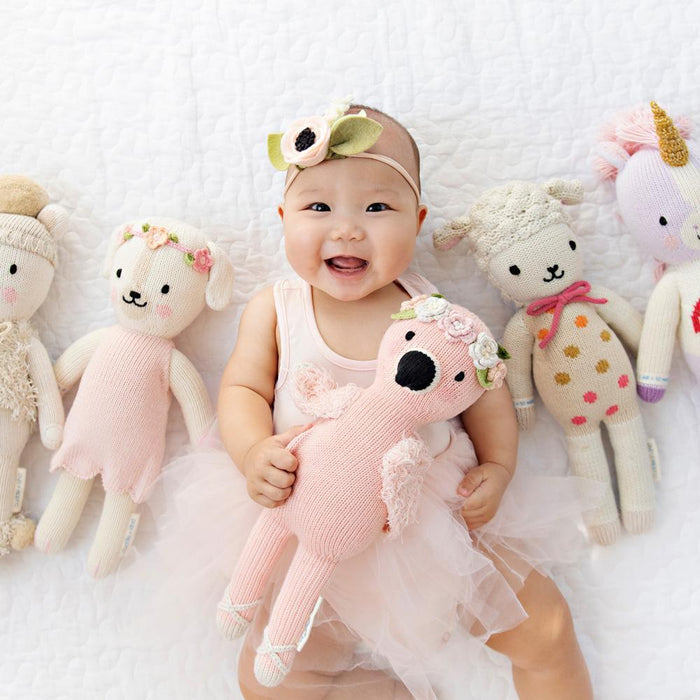 Baby smiling while holding Cuddle and Kind Penelope the Flamingo