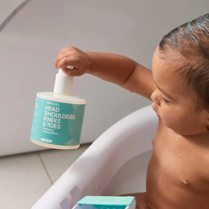 Baby holding Frida Head, Shoulder, Knees and Toes Shampoo + Body Wash while taking a bath