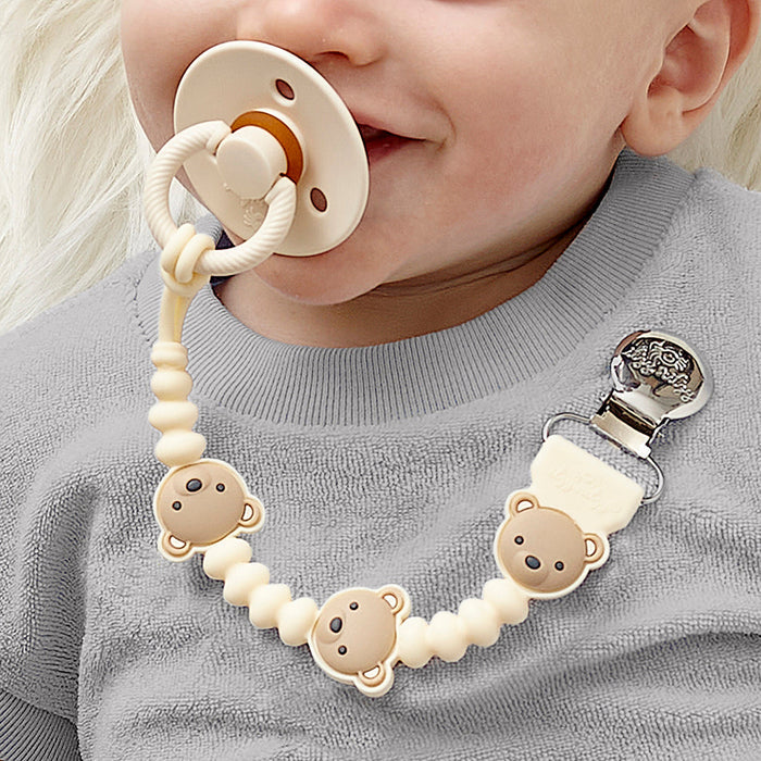 Baby sucks on pacifier attached to Itzy Ritzy Sweetie Strap Plus - Theo the Bear