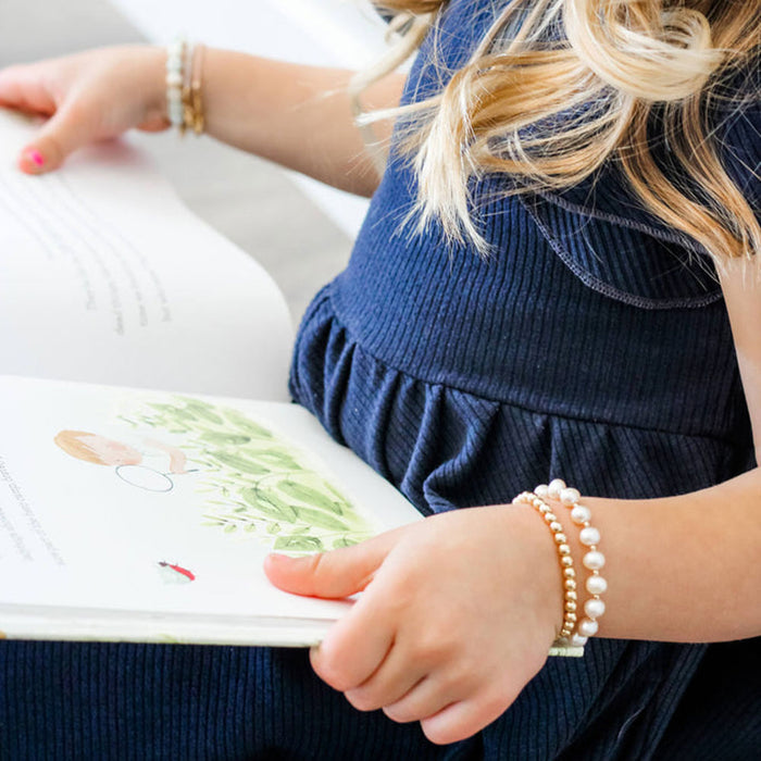 Little girl reads book while wearing Joyful Bead Company Fancy Pearl Bracelet