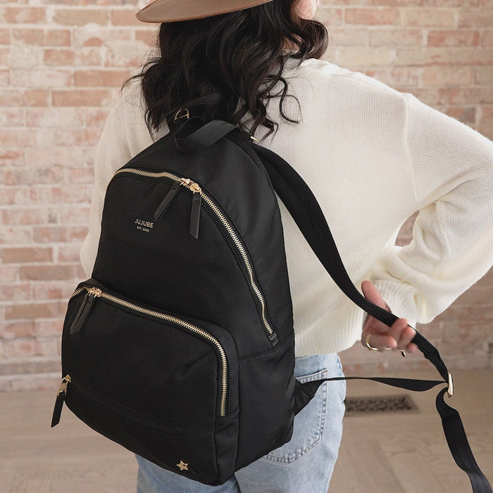 Woman puts on JuJuBe Everyday Backpack - Black