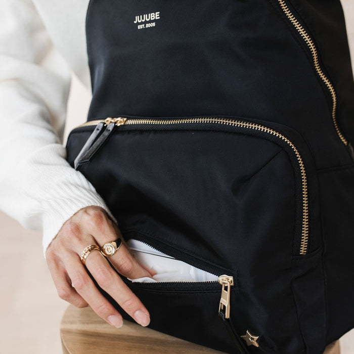 Woman reaches into front pocket of JuJuBe Everyday Backpack - Black