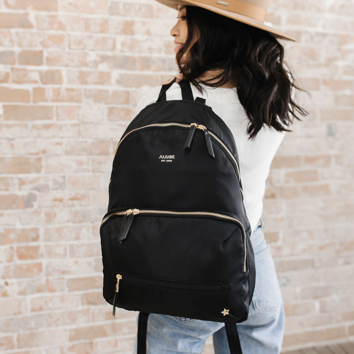 Woman holds JuJuBe Everyday Backpack - Black over her shoulder