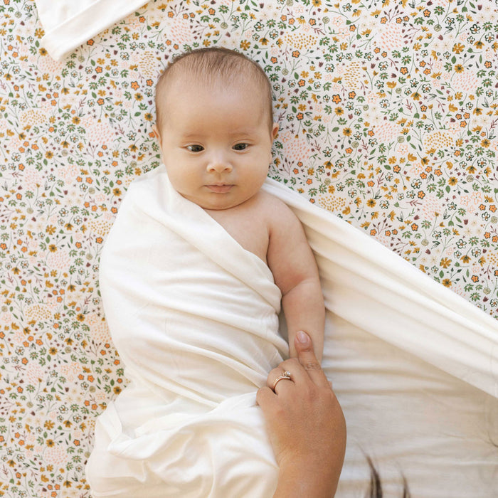 Baby lying on Little Unicorn Stretch Knit Crib Sheet - Pressed Petals