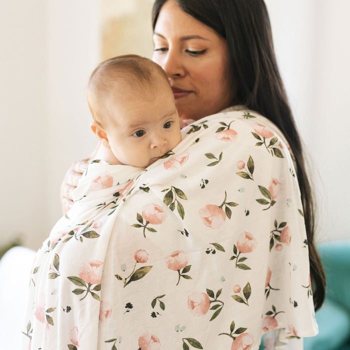 Mom holding baby wrapped in Little Unicorn Stretch Knit Swaddle Blanket - Watercolor Roses