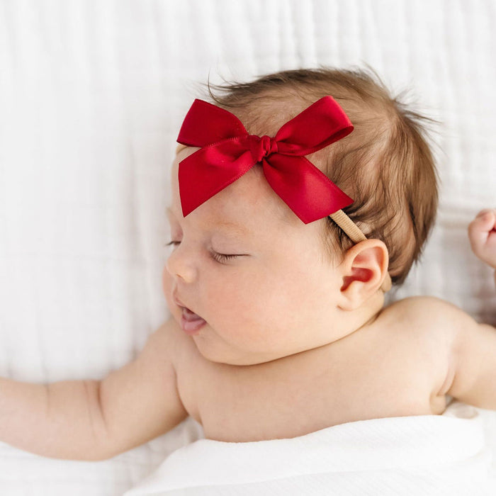 Baby wearing red bow from Lou Lou and Company Satin Bow Headband 3 Pack - Small - Champagne / Ruby / Evergreen
