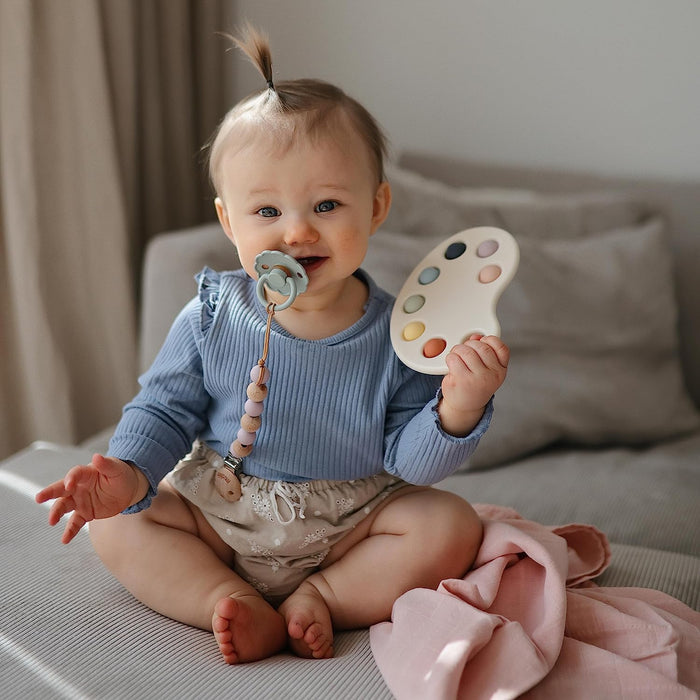 Baby girl plays with Mushie Paint Palette Press Toy