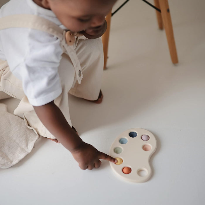 Little boy plays with Mushie Paint Palette Press Toy