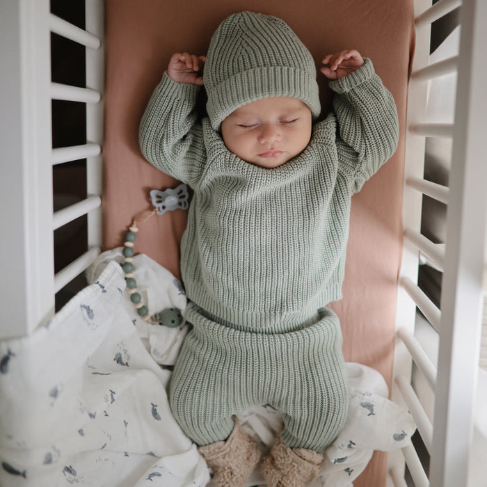Baby sleeping next to Mushie Silicone Pacifier Clip - Luna - Dried Thyme