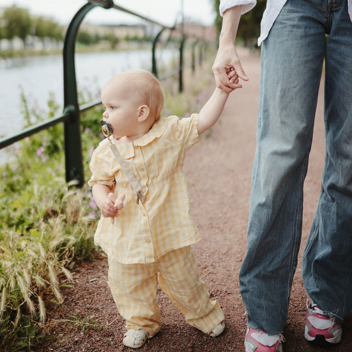 Baby girl holds moms hand while carrying Mushie Unicorn Figurine Teether - Blush