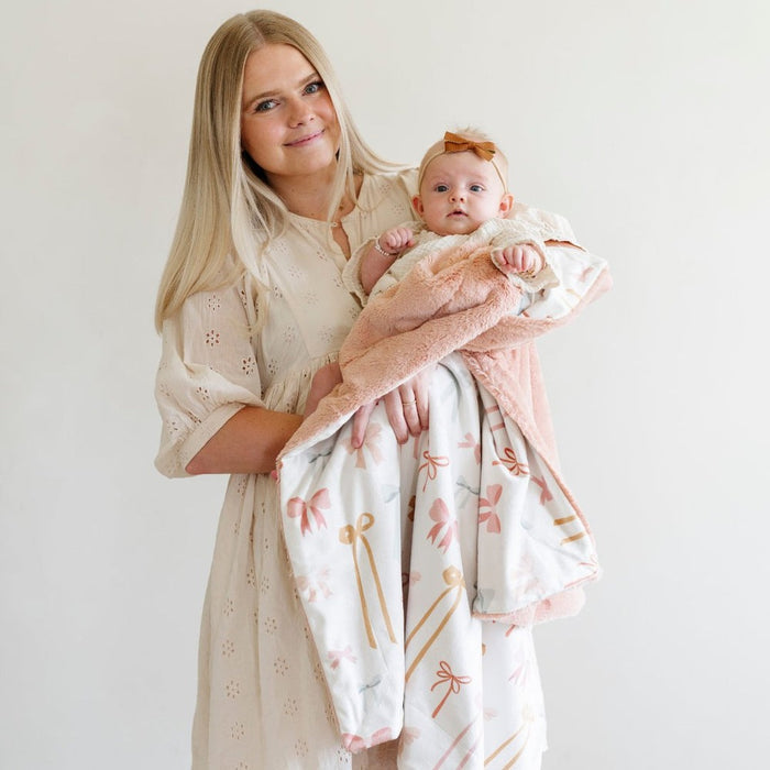Mom holds baby wrapped in Saranoni Receiving Minky / Lush Blanket - Bows