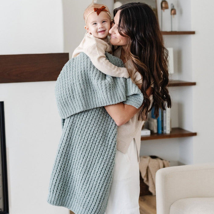 Mom holds baby girl wrapped in Saranoni Receiving Waffle Knit Blanket - Elm
