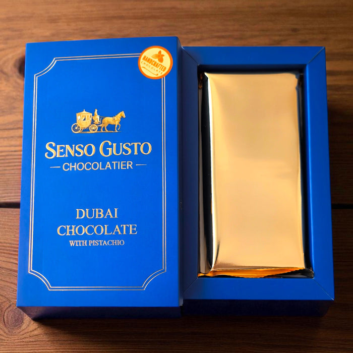 Gold Dubai chocolate bar with pistachio and kunafah in a premium blue 'Senso Gusto Chocolatier' box on a wooden surface
