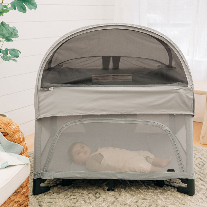 Baby lies in REMI playard with attached UPPAbaby REMI Playard Canopy