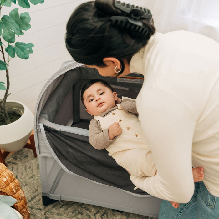 Mom lifts baby out of REMI playard with UPPAbaby REMI Playard Canopy attached