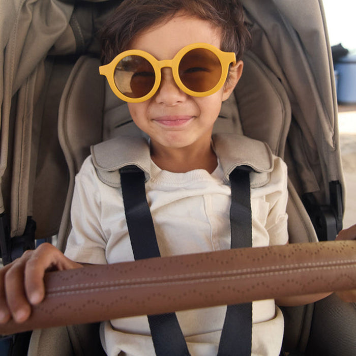 Child wearing sunglasses smiles while riding in Veer Switchback with Veer Switchback Seat Bumper Bar Leather Grips - Genuine Napa Leather - Saddle attached